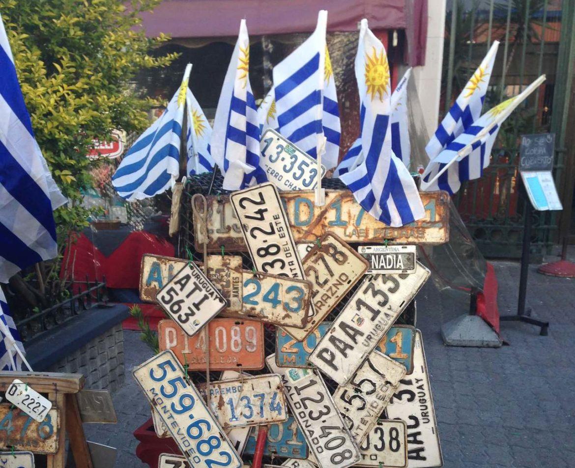 alte Nummernschilder aus Uruguay auf einem Ständer, darüber mehrere Uruguay-Flaggen